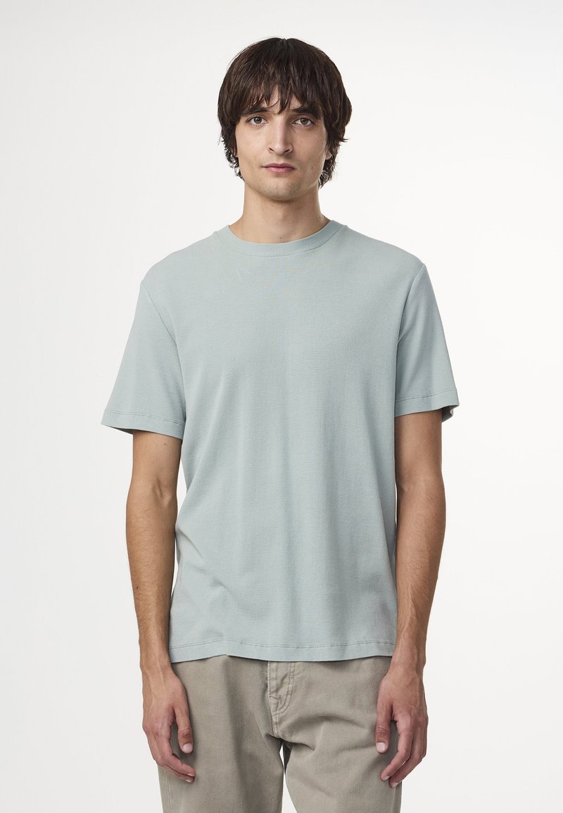 T-shirt azzurro chiaro a maniche corte con scollatura rotonda. Il tessuto sembra morbido con una vestibilità rilassata. Indossato con pantaloni chiari.