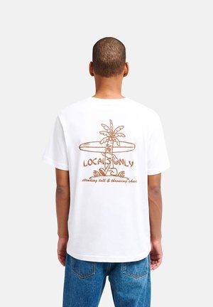 Uomo che indossa una maglietta bianca con grafica marrone di palma e tavola da surf e il testo "Local Only" sulla schiena, abbinata a jeans blu.