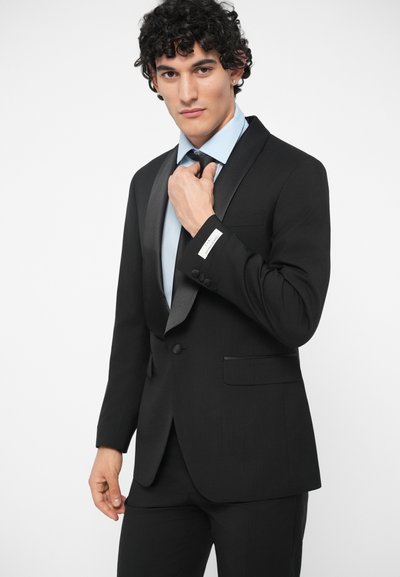 Černé smokingové sako se saténovými klopami a zapínáním na jeden knoflík. Nosené přes světle modrou košili, má jemný detail kapsy.