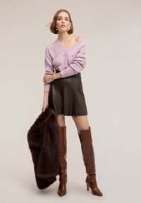 Maglione lavorato a maglia di colore lilla chiaro con scollo a V, minigonna in pelle nera, scialle in pelliccia marrone e stivali stiletto marroni al ginocchio.