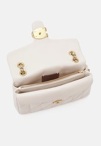 Kremowa pikowana skórzana torebka otwarta, aby pokazać złote okucia, wewnętrzną kieszeń na zamek oraz pętle na łańcuch pod klapą.