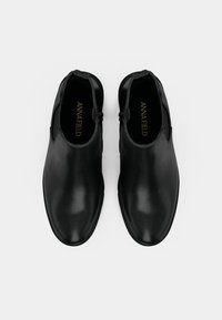 Svarta läderankelboots med slät textur, rundad tå, sidodragkedja och subtil logga på innersulan.