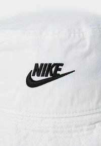 White bucket hat made of soft canvas, featuring a prominent black embroidered Nike logo with a curved swoosh design.