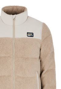 Veste en polaire beige avec un col haut, une fermeture éclair à l'avant et une finition texturée et duveteuse. Présente un patch logo avec un design de montagne.