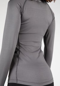 Grijze lange mouw sporttop met een aansluitende pasvorm, zachte textuur en subtiele naaddetails. Voorzien van een ronde hals en zijpanelen.