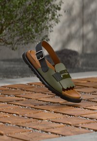 Πράσινο σανδάλι με υφή, μαύρα λουριά και ταμπά πάτο, με κυματιστό σχέδιο και γυαλιστερές λεπτομέρειες. Ελαστική σόλα για καλύτερη πρόσφυση.