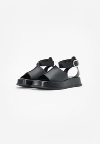Czarne sandały z odkrytymi palcami i piętą, z szerokimi paskami, regulowanym zapięciem na kostce oraz grubą, wyściełaną podeszwą. Gładkie matowe wykończenie.