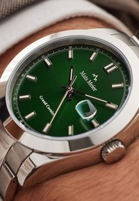 Montre en acier inoxydable avec un cadran vert, des index argentés et une fenêtre de date. Dispose d'un bracelet texturé et d'un détail de couronne proéminent.
