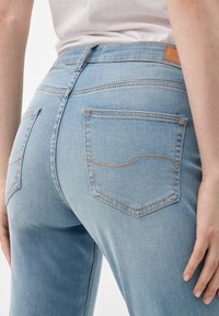 Jeans de denim azul claro con una cintura de altura media, que cuentan con dos bolsillos traseros y detalles de costura en contraste. La tela parece ligeramente desgastada.