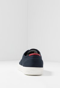 Marinefarbene Leinensneaker mit weißer Gummisohle, rotem Akzent an der Ferse und strukturiertem Obermaterial. "TOMMY HILFIGER" auf der Ferse eingeprägt.