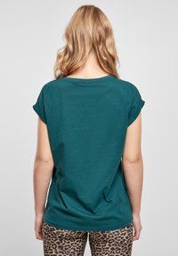 Teal bomulls t-shirt med uppvikta ärmar, rund halsringning och avslappnad passform, kombinerad med leggings i leopardmönster. Slät textur, avslappnad design.
