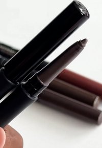 Ensemble de quatre crayons eyeliner avec un emballage noir. Le liner avant a une pointe fine et une couleur brun foncé, les autres présentent différentes nuances de brun.