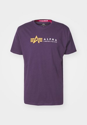 Lilla bomulds t-shirt med et gult "A" logo og teksten "ALPHA INDUSTRIES" i hvid. Korte ærmer og rundt halsudskæring.