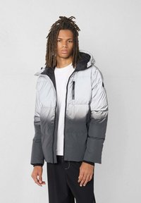 Grijze donsjas met een verloopontwerp, voorzien van een capuchon, ritssluiting aan de voorkant en een borstzak. Gladde textuur met een glanzende afwerking.