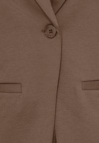 Tissu de blazer marron avec un bouton visible fermé et deux poches à fente horizontale de chaque côté à l’avant.