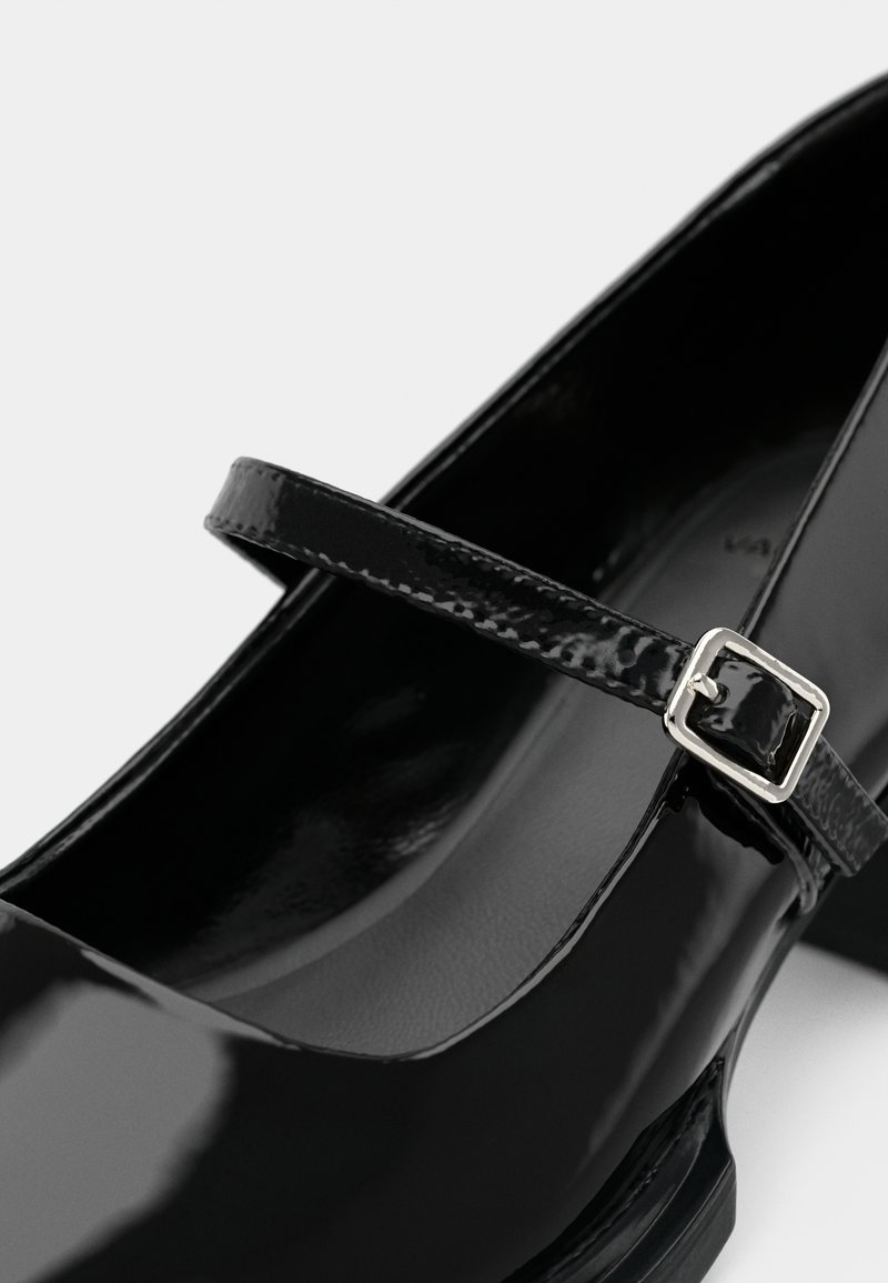Schwarzer Lacklederschuh im Mary Jane-Stil mit einem dünnen Riemen und silberner Schnalle, mit runder Zehe und glatter, glänzender Oberfläche.