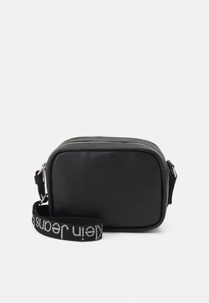 Sac bandoulière rectangulaire noir avec fermeture éclair argentée et sangle noire amovible portant le texte blanc "Calvin Jeans".