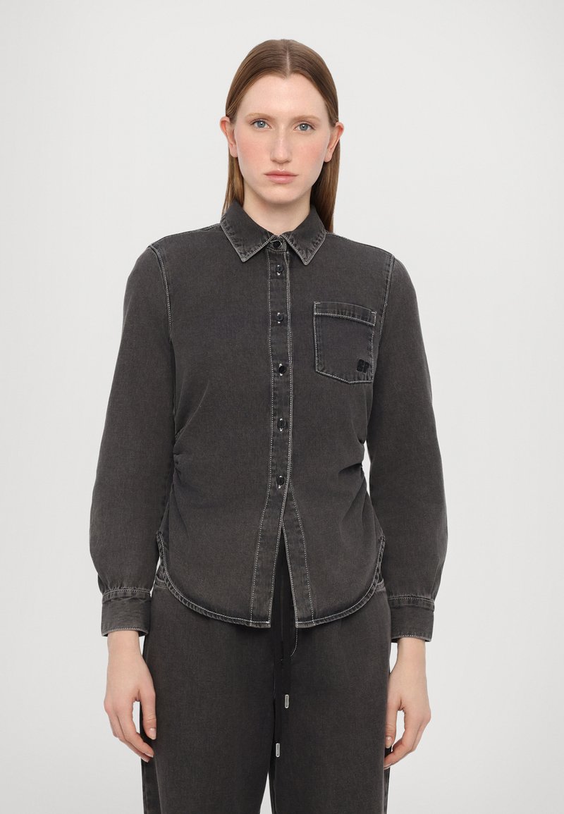 Camisa de denim preto com frente de botões, gola pontiaguda, mangas longas, um bolso no peito e detalhes de costura em contraste.