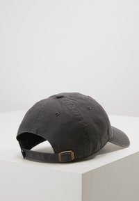 Gorra de béisbol de algodón gris oscuro con visera curvada, cierre de metal ajustable y textura suave. La vista trasera muestra la costura y los agujeros de ventilación.