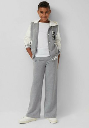 Sweat-shirt gris avec des manches blanches arborant la lettre "S" et un T-shirt blanc en dessous. Pantalon de survêtement gris à jambes larges et baskets blanches.