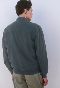 Leichte, dunkelgrüne Bomberjacke mit einem Reißverschlusskragen. Verfügt über gerippte Bündchen und Saum, eine glatte Textur und ein minimalistisches Design.