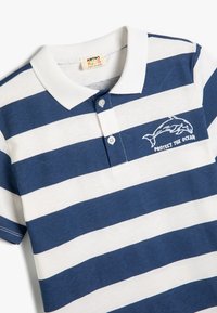 Marineblå og hvidstribet polo med krave, der har et delfinmotiv og teksten "BESKYT HAVET" broderet i hvidt.