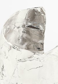 Scultura metallica argentata con superficie testurizzata e irregolare e bordo superiore frastagliato, che riflette la luce ed esibisce opacità variabile.