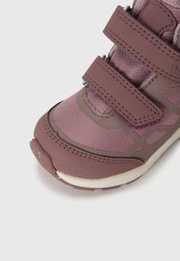 Sapatilha atlética roxa com parte superior em malha e sintético, duas correias de velcro, acentos cosidos e uma sola de borracha ligeiramente texturizada.