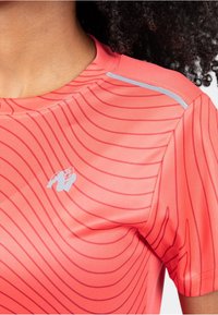 Koraal sportshirt met gebogen rode strepen, korte mouwen en een reflecterende accent op de schouder. Logo bedrukt op de borst.