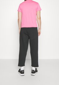 Kort rosa t-shirt med korta ärmar, kombinerad med lösa svarta byxor med vita sidostråk och svarta träningsskor.