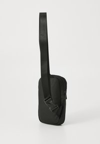 Sac bandoulière noir avec fermeture éclair et sangle réglable, positionné verticalement sur un fond blanc uni.