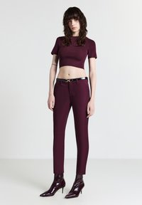 Top corto color bordeaux e pantaloni slim-fit abbinati, con una cintura nera dotata di un accento dorato. Stivaletti neri lucidi completi l'outfit.