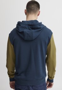 Felpa con cappuccio caratterizzata da un corpo blu e maniche verde oliva, realizzata in tessuto morbido con orlo e polsini a costine.