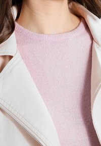 Heller rosa gestrickter Pullover mit weicher Textur, kombiniert mit einer weißen Lederjacke mit Reißverschluss und Reverskragen.