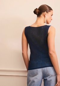 Débardeur sans manches bleu marine avec un motif texturé agrémenté d'accents scintillants. Associé à un jean taille haute bleu clair. Tissu lisse et décolleté arrondi.