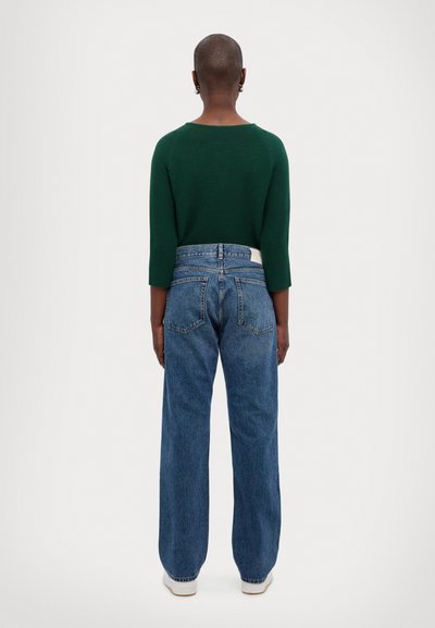 Green ribbed knit sweater, three-quarter sleeves, paired with high-waisted, wide-leg blue denim jeans. White label on jeans' back waistband.