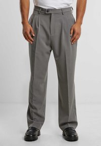 Pantalones gris de plisado, hechos de una tela suave, con cierre de botón, bolsillos laterales y un diseño de pierna recta. Combinados con zapatos negros.