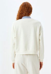 Crème-kleurige sweatshirt met een losse pasvorm, ribgebreide manchetten en een cropped zoom. Gestructuurde stof, lijkt zacht met een gladde oppervlakte.