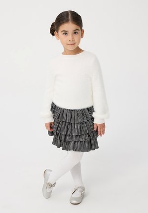 Maglione bianco soffice con maniche lunghe, gonna a strisce nere e grigie con volant, collant bianchi e ballerine argentate lucide con dettagli a fiocco.