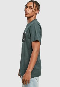 Dark green cotton t-shirt with short sleeves, crew neck, and a front graphic print. The fabric appears soft with a relaxed fit.