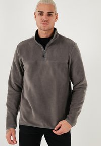 Grå fleece pullover med halv-zip krave, der har lange ærmer og en glat tekstur. Udsmykket med kontrastsyninger og en afslappet pasform.