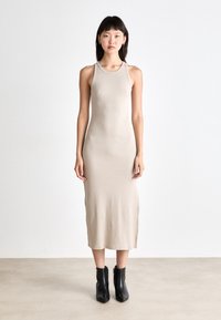 Rochie midi bej, ajustată pe corp, cu decolteu rotund și design fără mâneci, realizată dintr-un material neted; modelul este accesorizat cu botine negre până la gleznă.