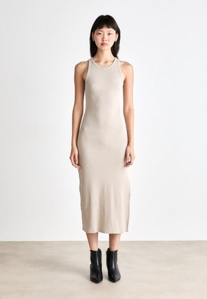 Beige, form-fitting midi dress with a round neck and sleeveless design, made of smooth fabric; model paired with black ankle boots.