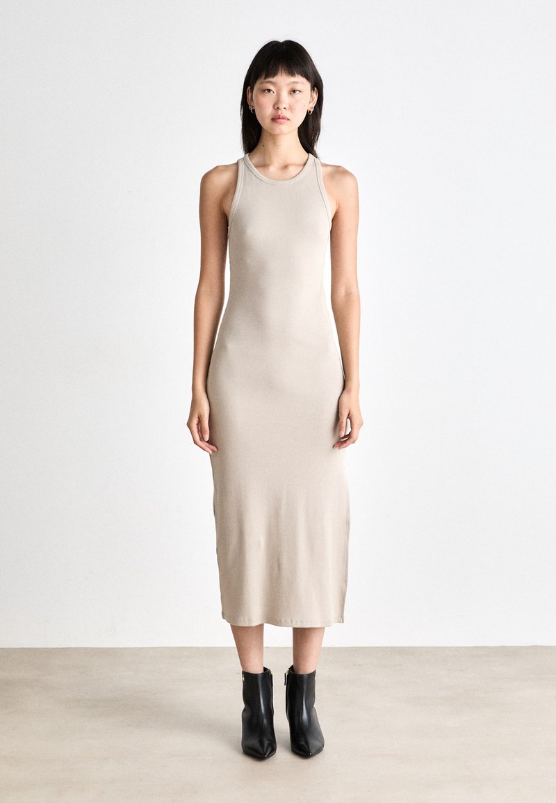 Rochie midi bej, ajustată pe corp, cu decolteu rotund și design fără mâneci, realizată dintr-un material neted; modelul este accesorizat cu botine negre până la gleznă.