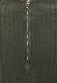 Falda de pana verde con canalones verticales, que cuenta con una cremallera plateada central. Textura suave, diseño hasta la rodilla y forma ajustada.