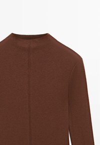 Bruine langermige top met een hoge hals en geribbelde textuur. Heeft een rugnaaddetail, eenvoudig ontwerp zonder versieringen.