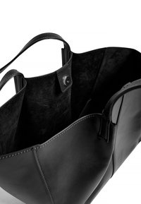 Svart läder tote-väska med mjukt mockainteriör, med två handtag, en platt botten och ett tryckknappslås. Slät utsida med diskret sömnad.