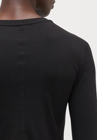 Black long-sleeve shirt with a round neckline, featuring a ribbed texture and visible stitching along the back seam.