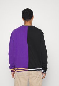 Bluza z okrągłym dekoltem z podzielonym wzorem w fioletowe i czarne sekcje. Żebrowany kołnierz i dół bluzy z żółtymi i białymi paskami.