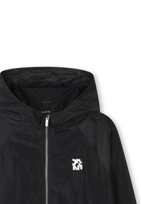 Giacca nera con cappuccio e zip frontale, realizzata in un materiale leggero. Presenta un rivestimento in rete e una piccola patch con logo sul petto.